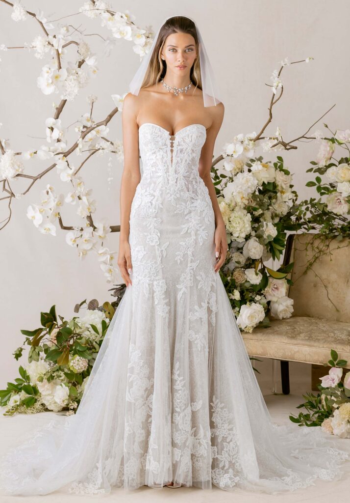 Our Celina wedding dress captures the intricate beauty of a pirouette. The strapless sweetheart neckline frames the décolletage with soft allure, leading into a plunging, boned bodice that sculpts and defines with intention. Layers of Chantilly lace are veiled beneath a delicate floral appliqué tulle overlay, creating movement and depth, while the godet skirt flares in a fluid, effortless sweep. Each step is a graceful extension of form, every curve imbued with poetic motion.