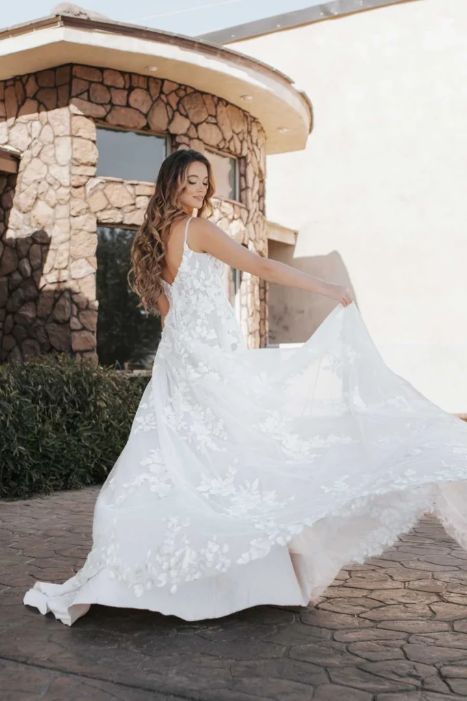 Sheer and elegant, features an allover matte floral lace that brings pure romance to the aisle. From sleek spaghetti straps, the sheer bodice highlights the figure with a soft V-neckline and subtle scoop back detail. From the waist, a flowing tulle A-line skirt moves freely, showcasing a gorgeous display of perfectly-placed lace appliqués throughout this wedding gown. For the final romantic touch, a timeless lace-edged shaped train sweeps behind for an idyllic walk down the aisle. This wedding dress is also available in plus sizes.