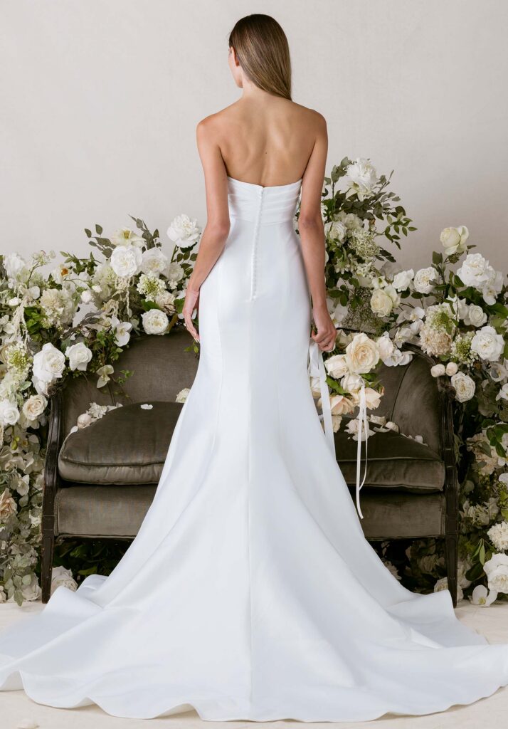Soft dimension meets sleek sophistication in our Lyren wedding dress. The strapless cat eye neckline frames the décolletage with angular elegance, while the draped empire waist bodice add subtle texture. Elongating princess seams trace the mermaid silhouette, lengthening your figure with graceful flow, while the structured faille fabric balances modern minimalism with effortless poise, creating a look that is both commanding and understatedly elegant.