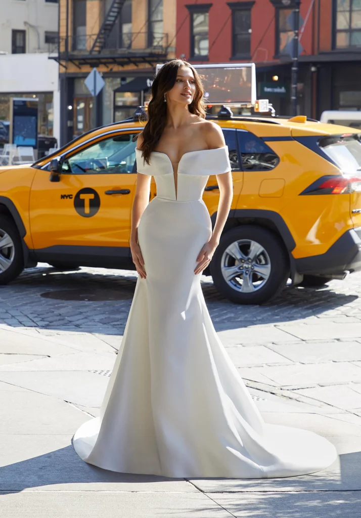 Clean and classic, our Sabine designer wedding dress has a timeless look in lustrous satin with its curve-hugging fit and flare silhouette. The bodice has a cuffed, off-the-shoulder neckline featuring a seductive plunge and perfectly placed seams to enhance the hourglass silhouette. Buttons down to the hemline add a touch of tradition and highlight the dramatic flare of the skirt.