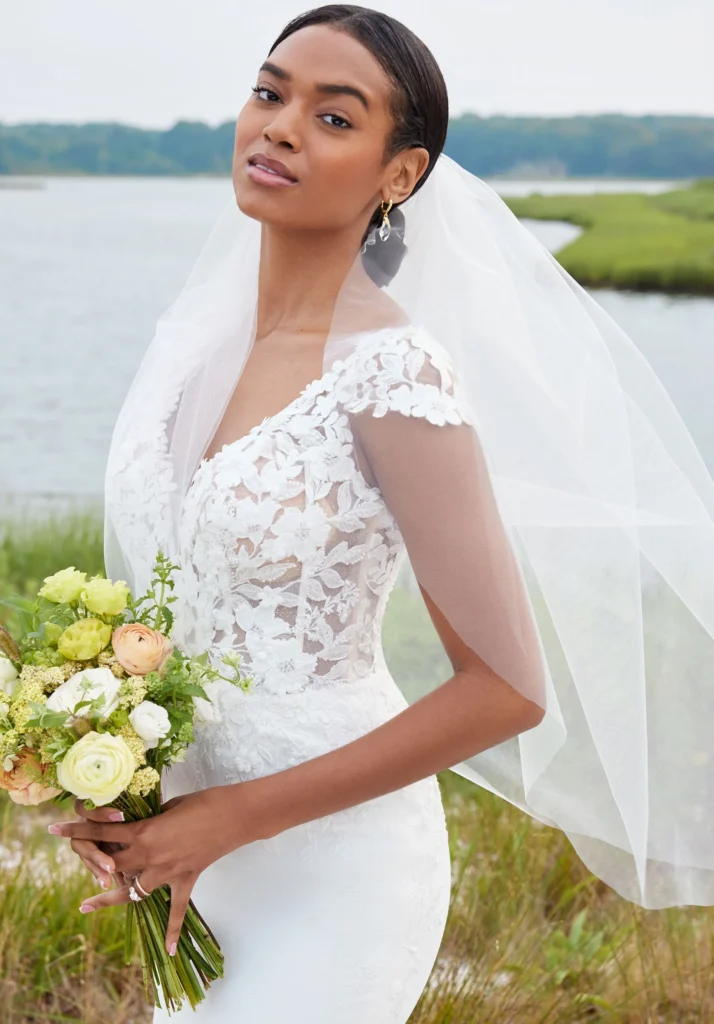 Our Shay designer wedding dress looks elegant and clean with our signature touches of romance. The bodice features a sculptured v-neckline and dainty cap sleeves designed with embroidered lace and three-dimensional floral appliqués, while the open back shows off the perfect amount of skin. The crepe skirt contours the body, gliding over your curves and leading to the breathtaking floral lace cutout train.