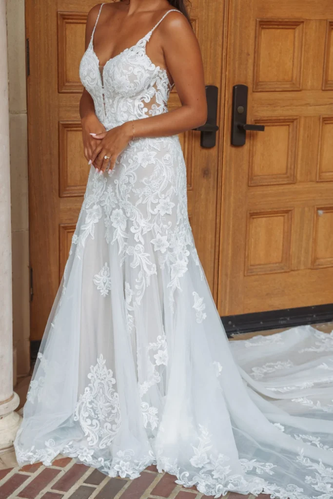 Sienna combines sexy bridal style with a timeless fit-and-flare silhouette. From elegantly thin beaded spaghetti straps, a plunging V-neckline splits the sheer bodice as graphic lace is intricately placed to accentuate the figure. A low scooped back meets a row of fabric covered buttons in the back that conclude at the hip. As scrolling graphic lace scatter past the hip into a frothy flared tulle skirt, the long shaped train of lace takes shape, creating an unforgettable wedding dress for the modern bride.