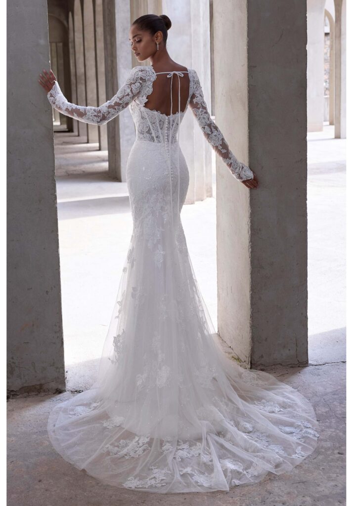 Striking and sculpted, our Vasiliki wedding dress features a sweetheart neckline with a seductive plunge on a structured corset bodice, balanced by the romance of detachable long sleeves. Lace appliqué and subtle sequins trace the fit and flare silhouette, catching light with every movement.