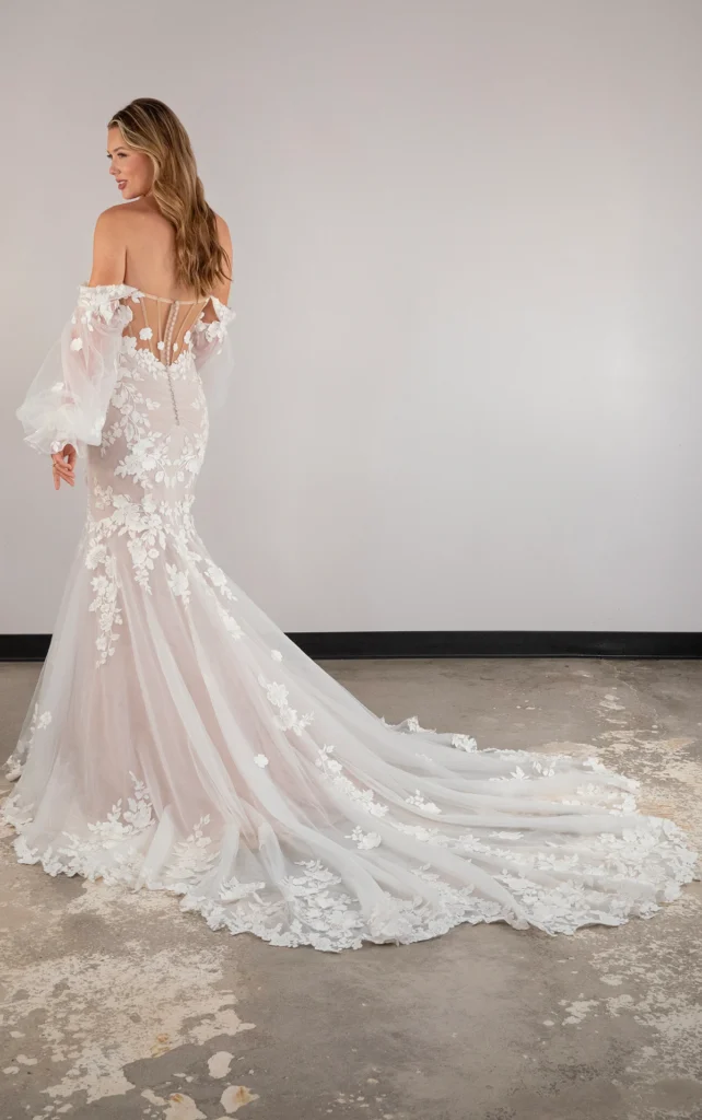 For an unforgettable bridal look, Paris offers high-fashion versatility with detachable sleeves that transform this off-the-shoulder bell sleeve wedding dress into a sexy strapless lace wedding dress in moments. The sheer blouson sleeves attach to a plunging sweetheart neckline and gather at the wrist for a free-spirited flowy effect. The ultra-fitted bodice accentuates the figure with discreet side cutouts that join a mesmerizing illusion corset back sealed with a row of timeless fabric-covered buttons. Floral lace appliqués scatter across the fit-and-flare silhouette as it extends into a frothy lace-trimmed skirt and train. Made for the modern romantic, this ethereal lace wedding gown captures the timelessness of that forever romance.